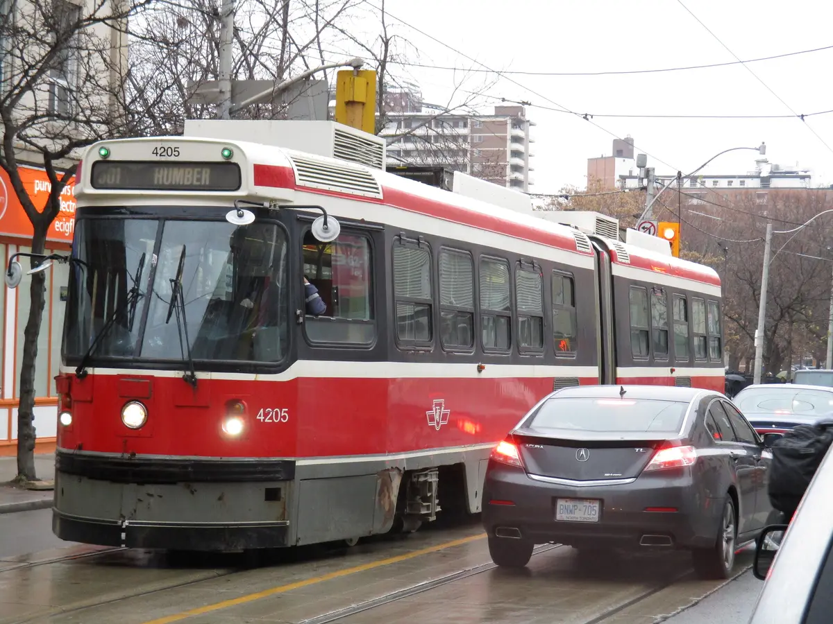 A red-and-white TTC streetcar on Queen Street with traffic close beside it