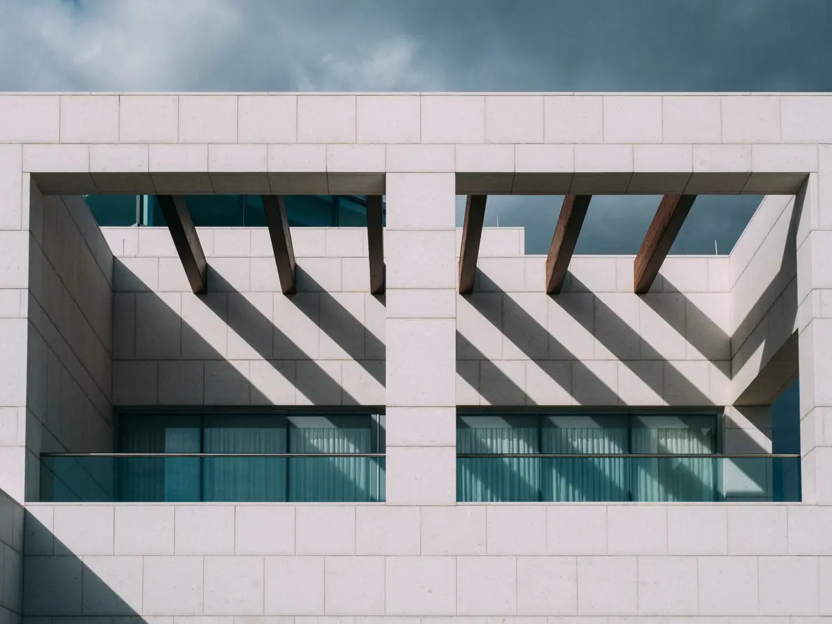 Pale stone walls of the Aga Khan Museum with angled timber beams casting long shadows under a stormy sky