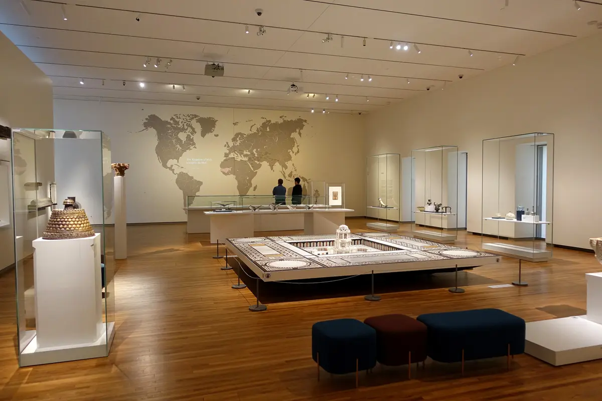 A gallery with a large wall map of the world, a model of a courtyard building under glass and cushioned benches