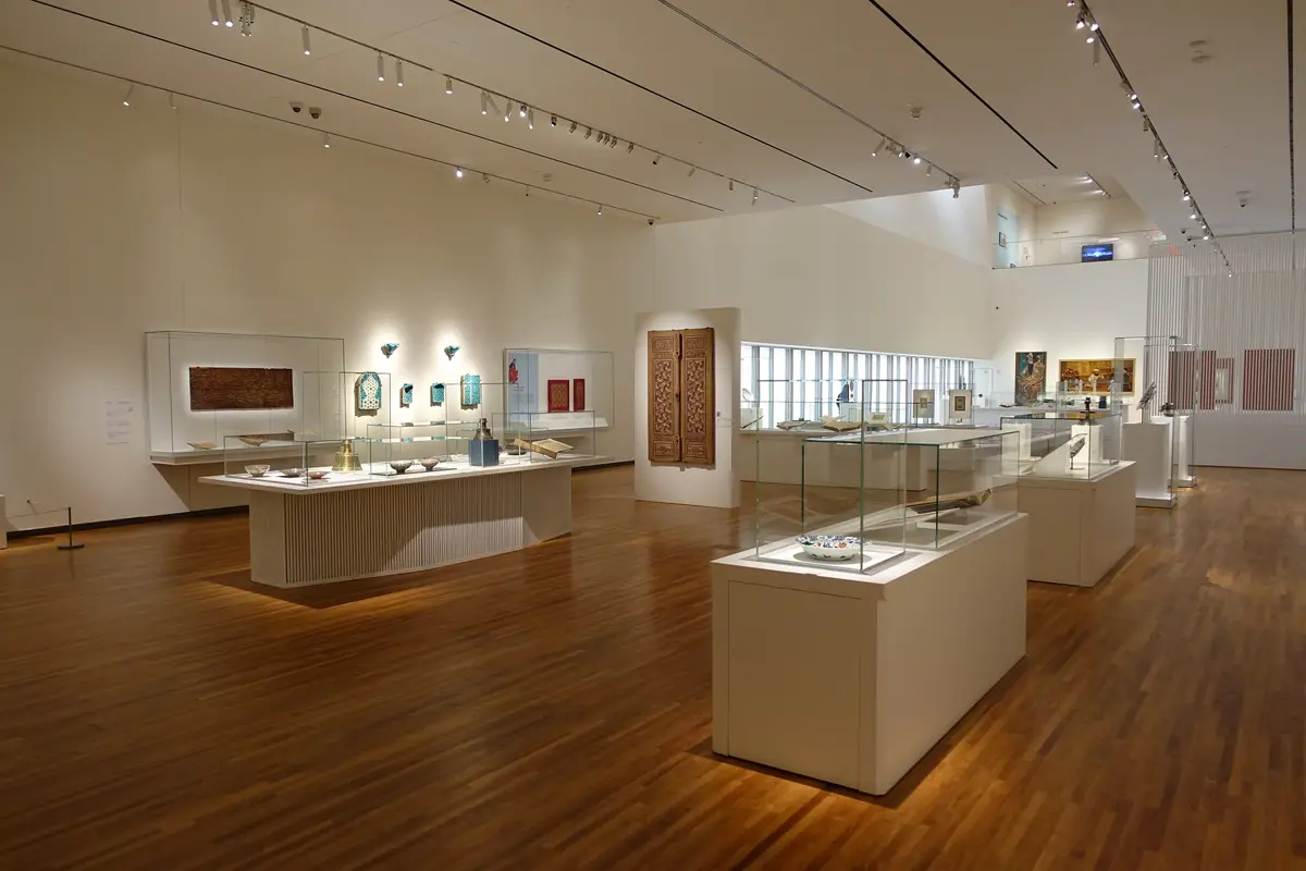 A bright gallery with display cases on a wooden floor and tall windows at the far end
