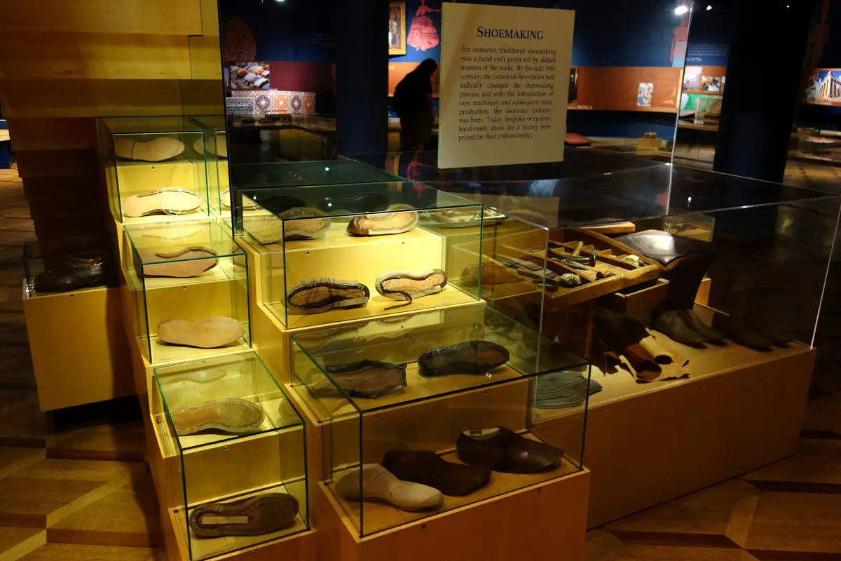 Glass cases of historic shoes and soles beneath a Shoemaking panel.