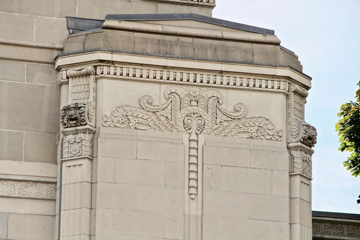 Close view of carved stone ornament with lion-head brackets on a pale stone building