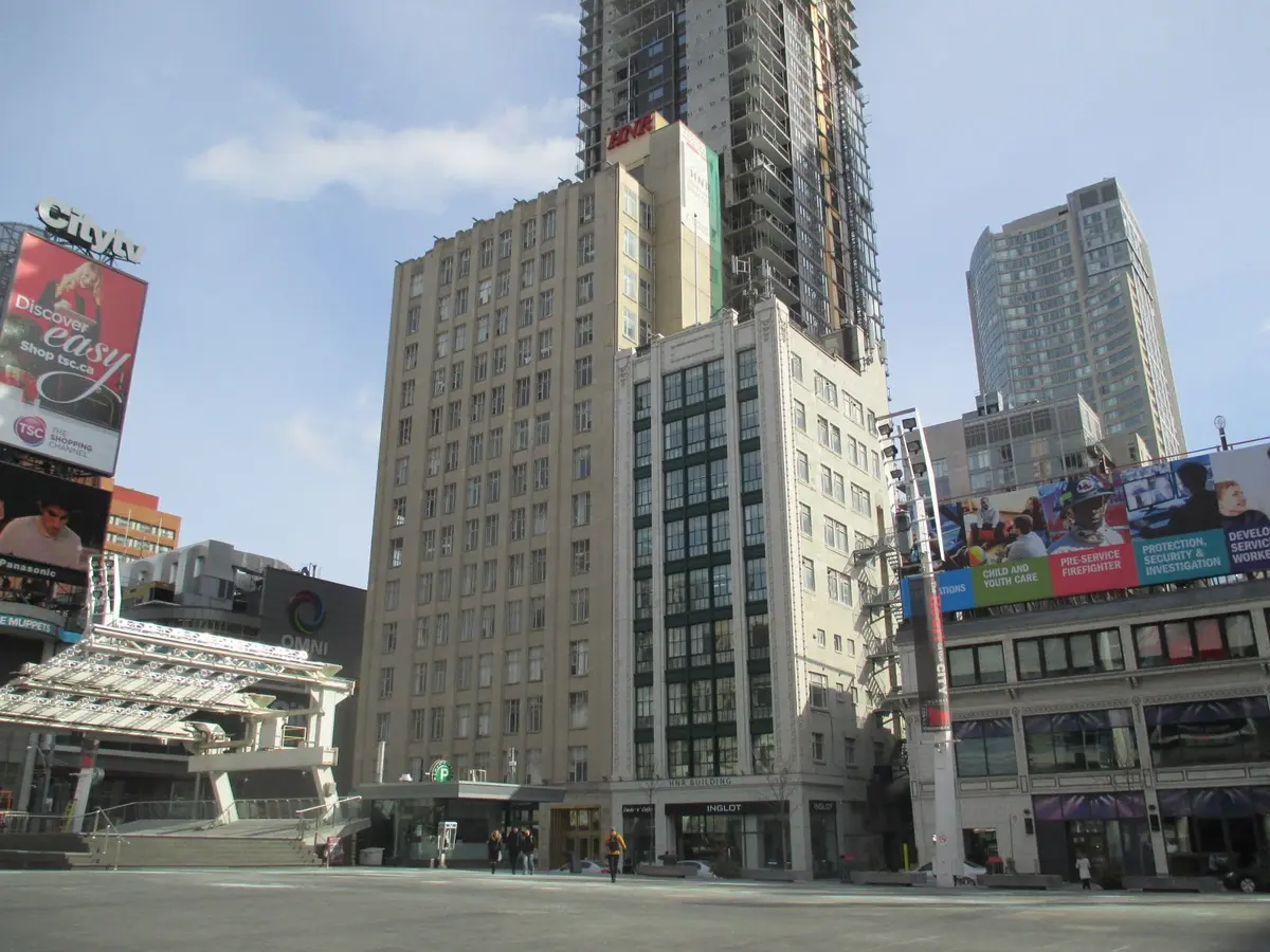 Tall stone-faced building with rows of windows and decorative panels beside a city street