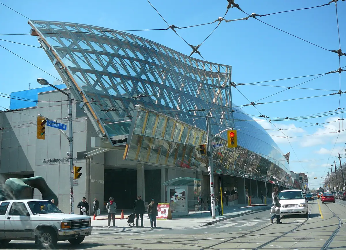 The curved glass and steel front of the Art Gallery of Ontario along Dundas Street West, with streetcar wires overhead and pedestrians at the crosswalk.
