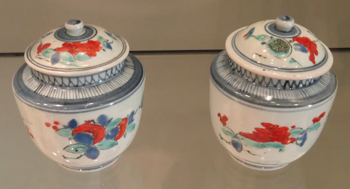 Two lidded porcelain jars painted with red, blue and green floral designs.