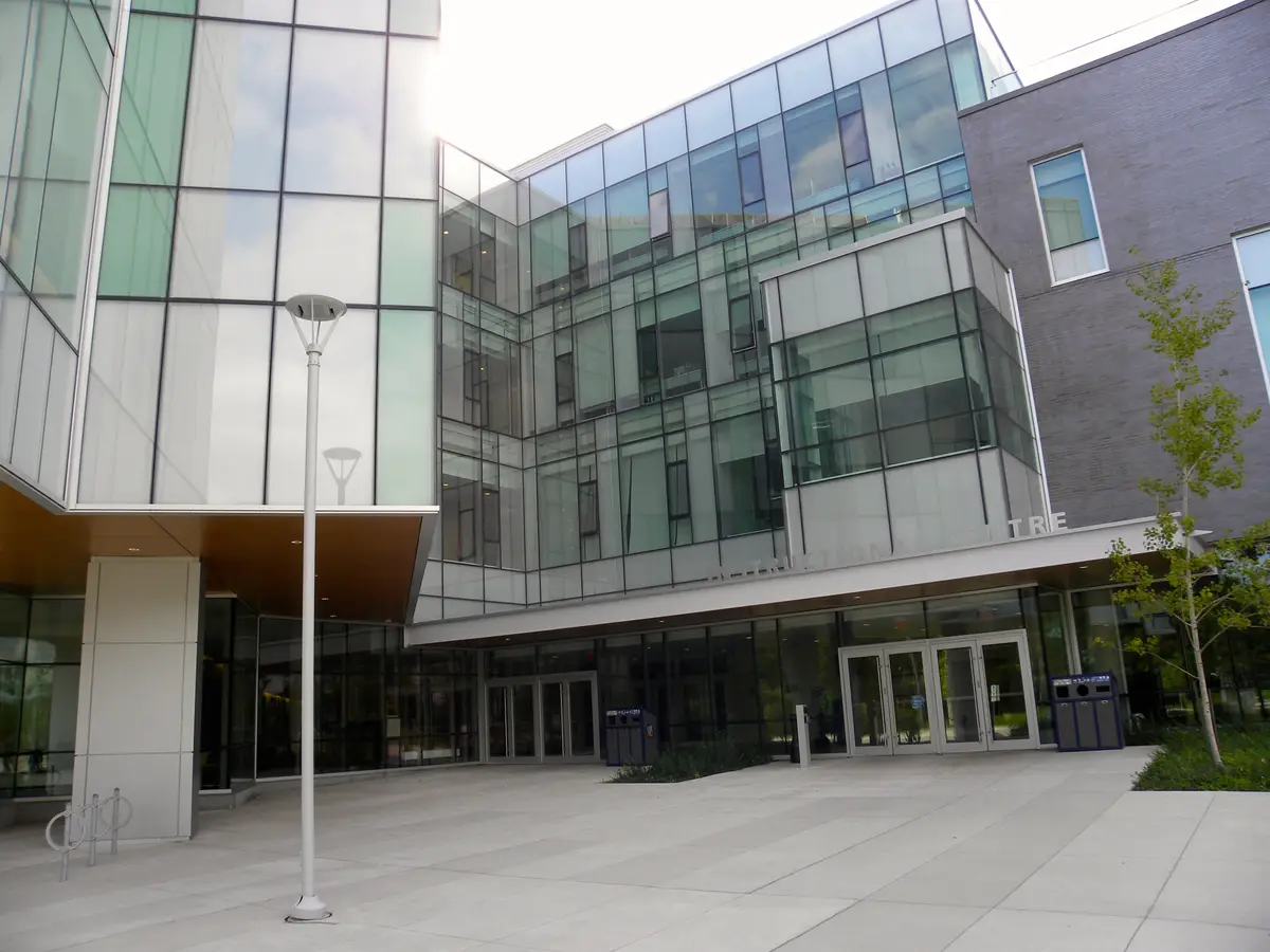 A glass and brick university building with a paved plaza and entrances at ground level.