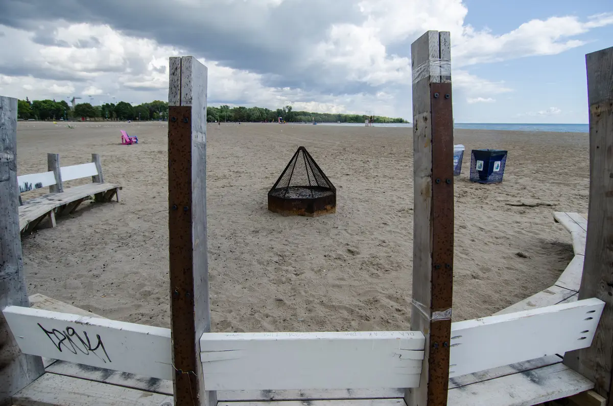 A wide sandy beach at Woodbine Beach, with weathered wooden posts in the foreground and the lake beyond