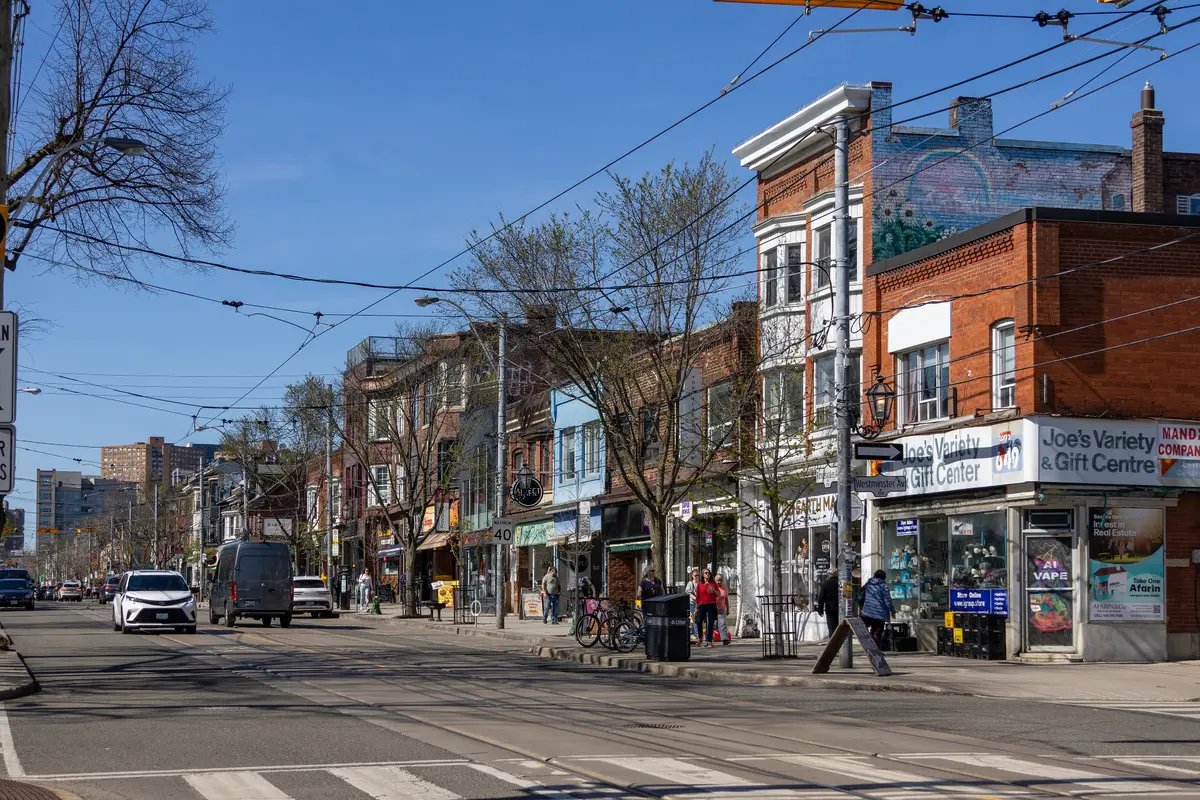 Roncesvalles Avenue on a sunny spring day, with brick shopfronts, people on the sidewalk and streetcar tracks in the road
