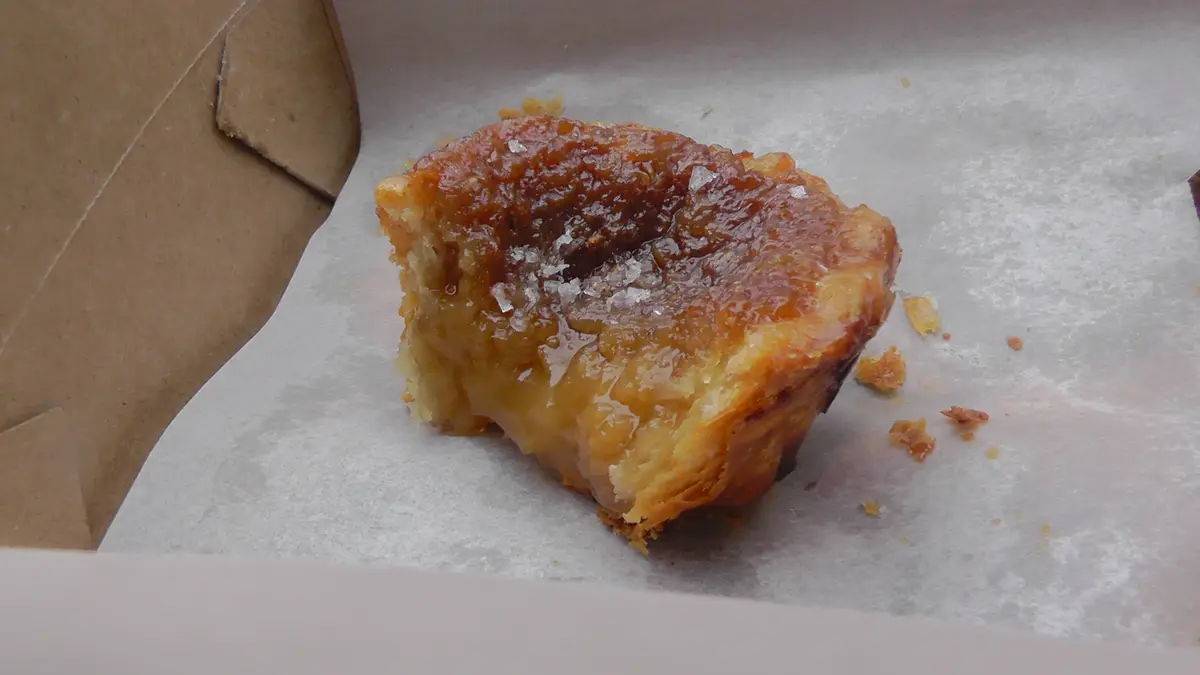 A butter tart bitten open on parchment paper, showing its glazed top and soft filling
