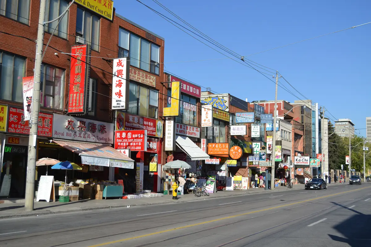 Shopfronts with red and yellow signs along a sunny stretch of Dundas Street West in Chinatown