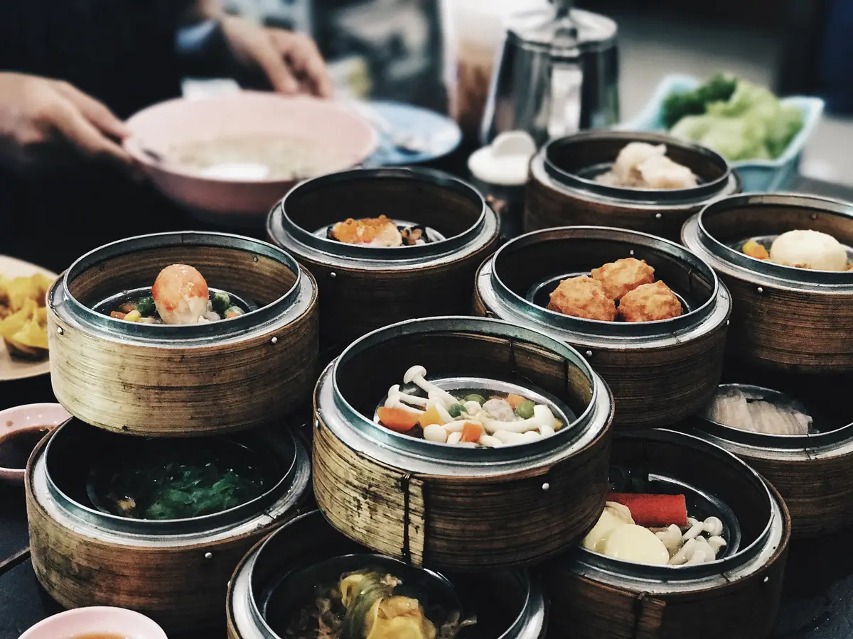 A table crowded with small bamboo steamer baskets of dim sum and a teapot