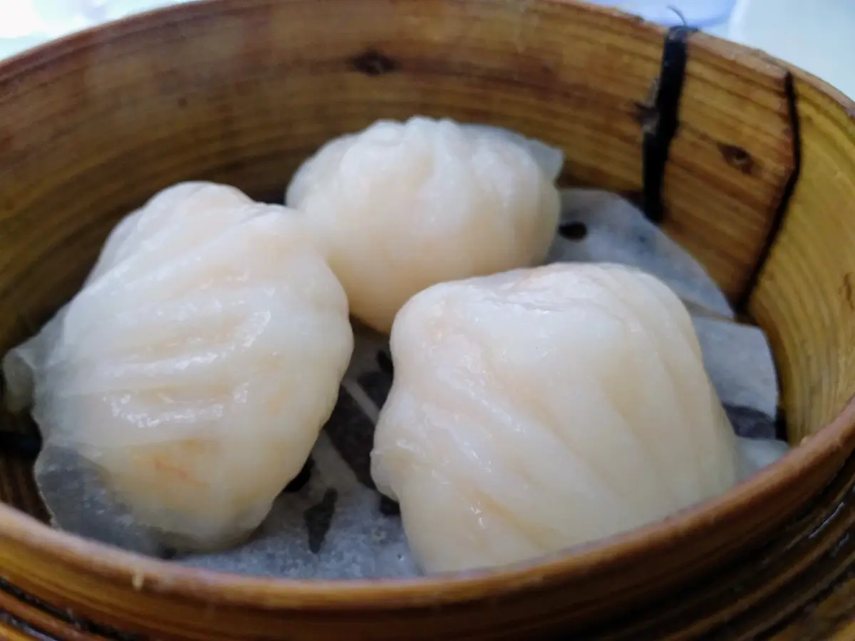 Three translucent dumplings resting in a bamboo steamer basket