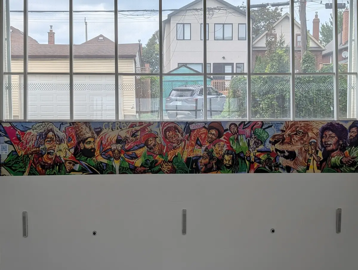 A colourful mural strip of musicians and a lion's head above a white wall inside a station