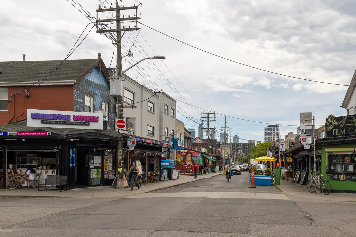 Shops with awnings and patios along Augusta Avenue under a tangle of overhead wires.