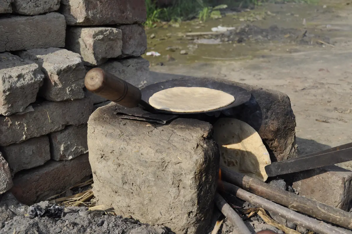 A roti cooking on a round iron tawa set over a clay stove, photographed in rural India