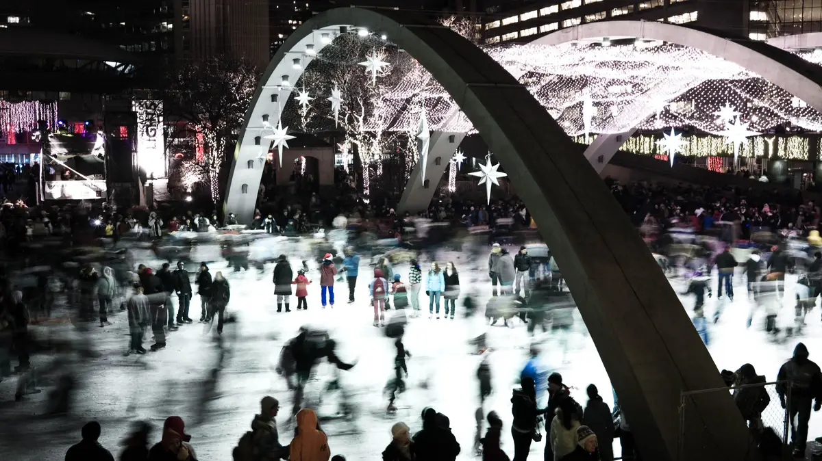 Skaters blurred in motion on the Nathan Phillips Square rink beneath a lit arch at night
