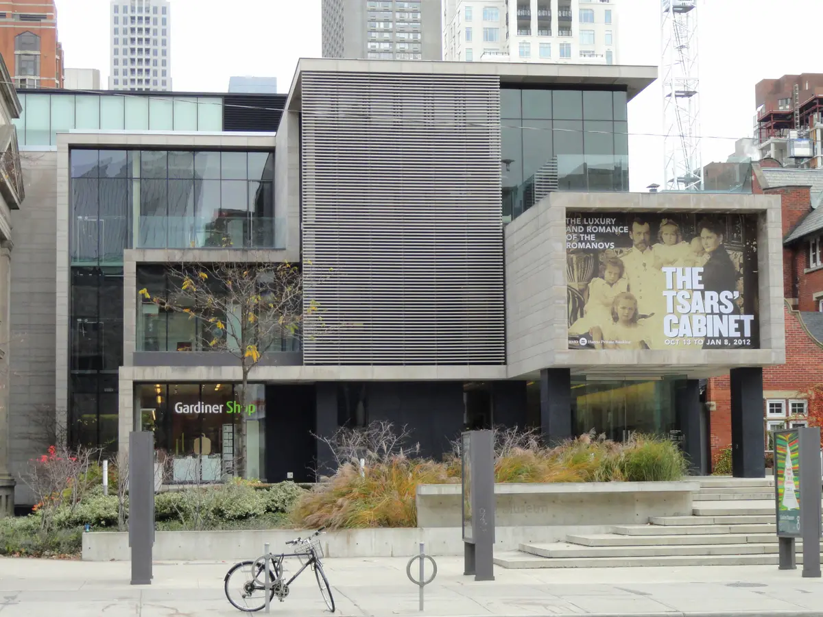 The concrete and glass front of the Gardiner Museum on Queen's Park, with a banner above the entrance and a bicycle locked out front.