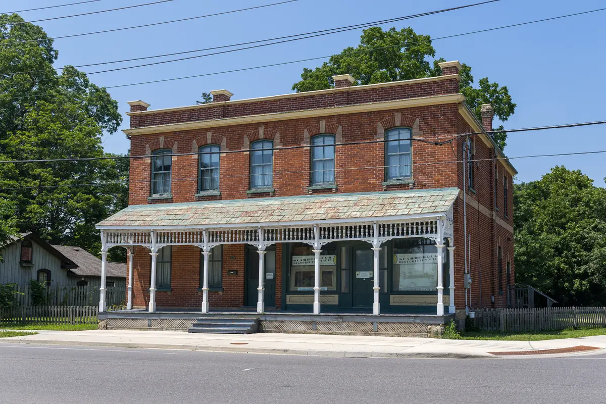 Two-storey red brick building with a long covered verandah beside Kingston Road in Scarborough, under a bright sky