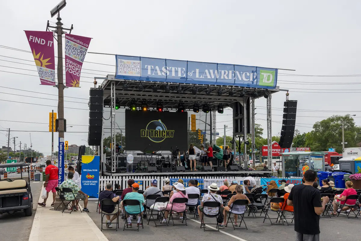 A stage with a blue Taste of Lawrence banner and rows of people sitting in folding chairs to watch