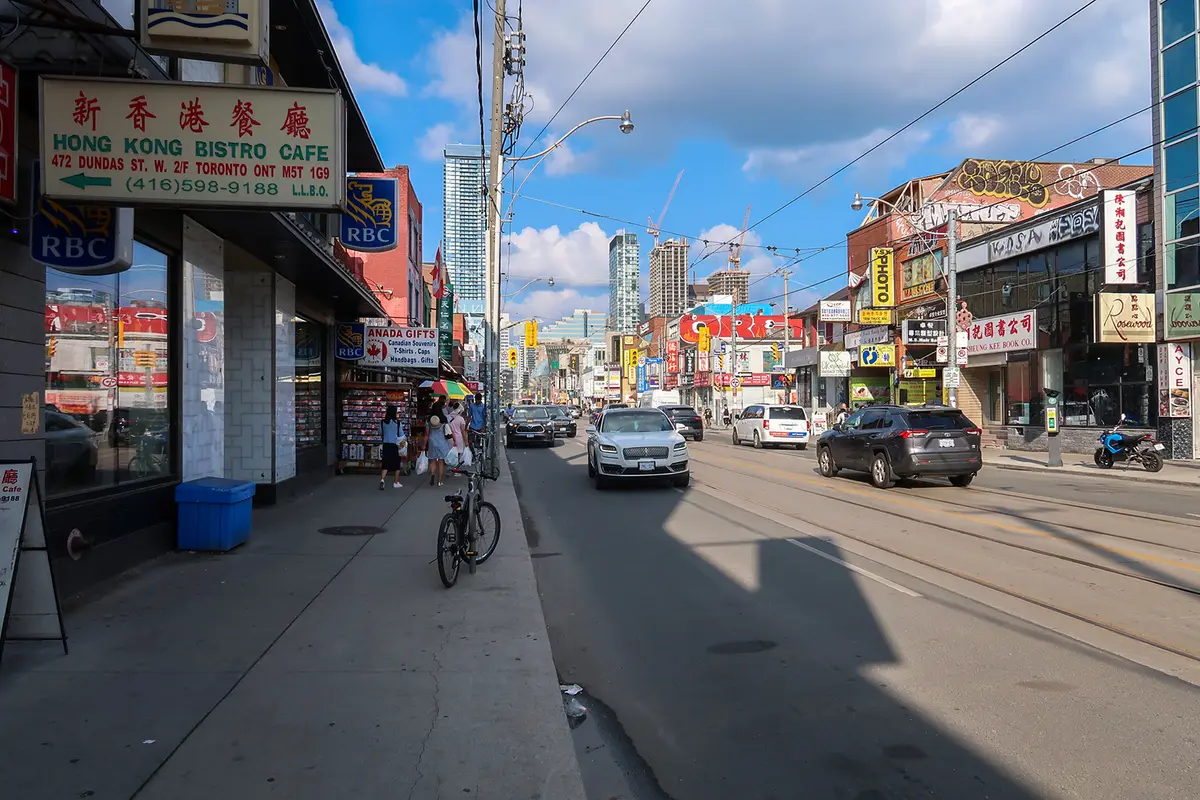 Red and yellow shop signs and storefronts along Dundas Street West in Chinatown, with traffic on the street.