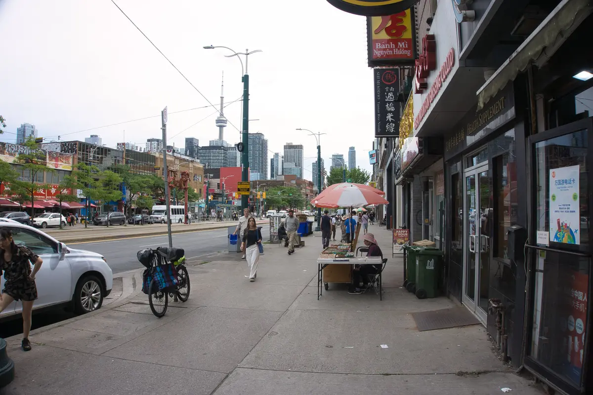 Shops, signs and pedestrians along Spadina Avenue in Toronto, looking south toward downtown towers.