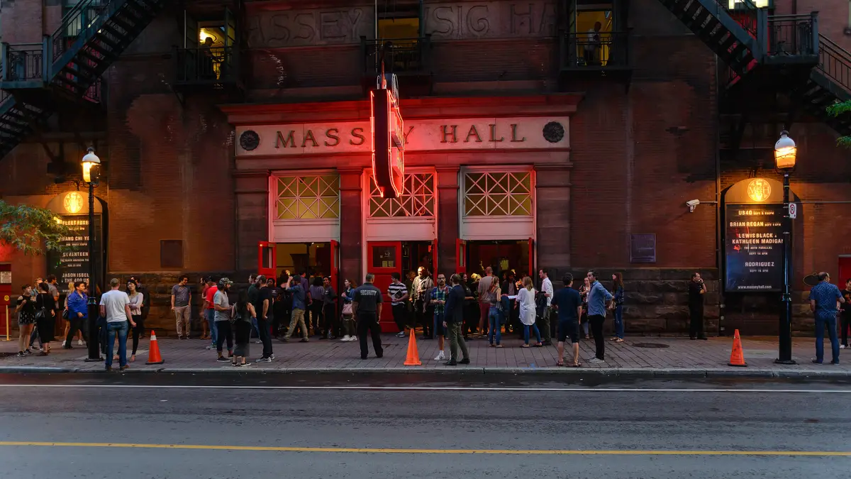 People gathered outside the lit front doors of Massey Hall on a summer evening