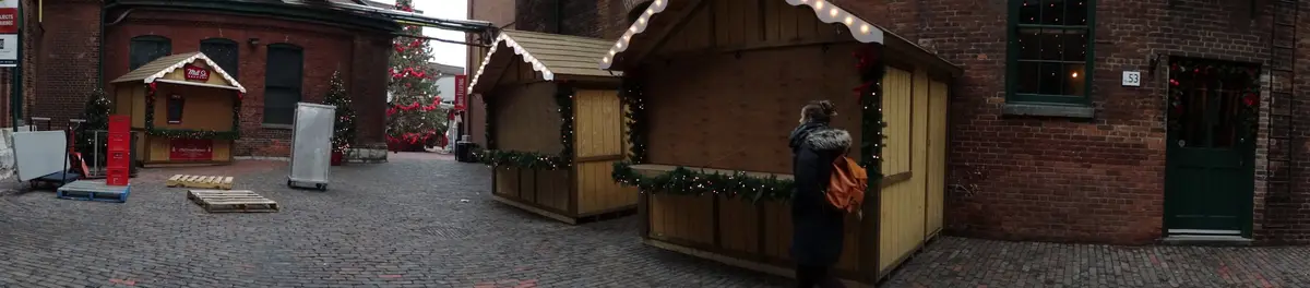 Wooden market stalls trimmed with garland and a decorated tree on a brick-lined lane in the Distillery District
