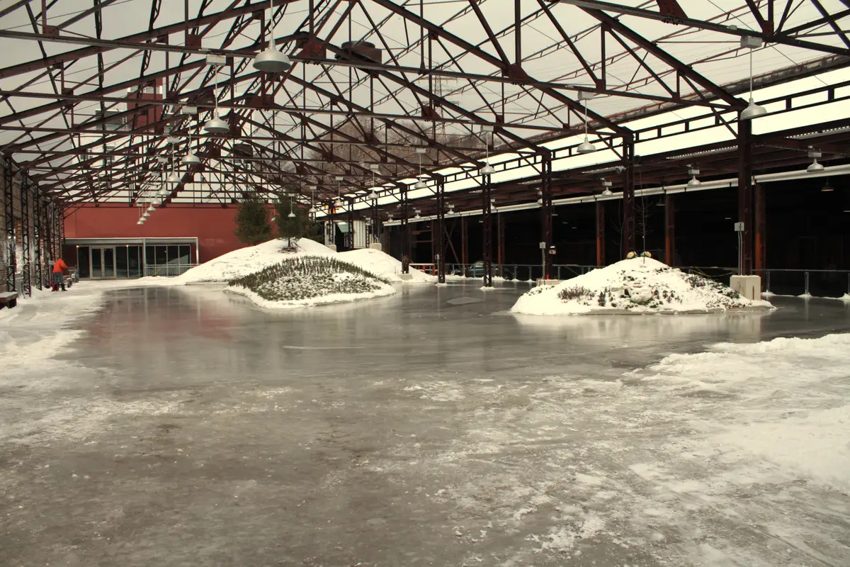 A covered skating rink under steel roof trusses at the Brick Works, with snow piled in the middle