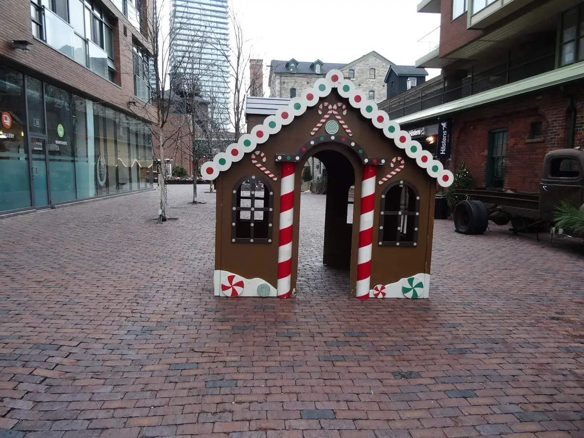 A gingerbread-house decoration with candy-cane columns on a brick-paved lane in the Distillery District