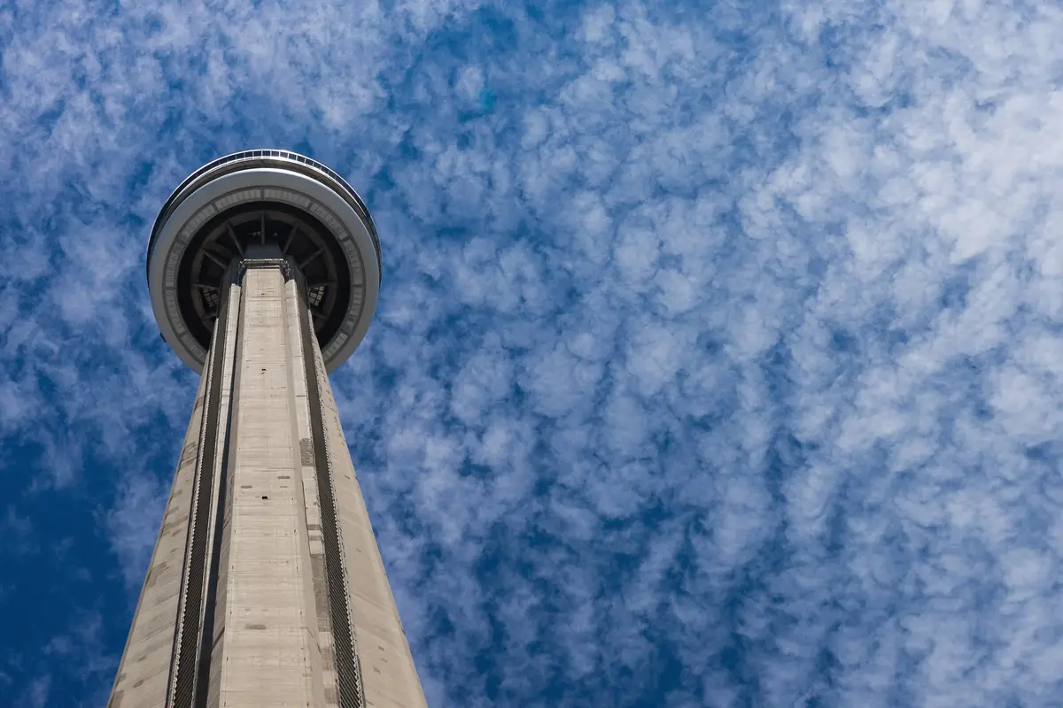The CN Tower's concrete shaft rising into a blue sky with wispy clouds, seen from below