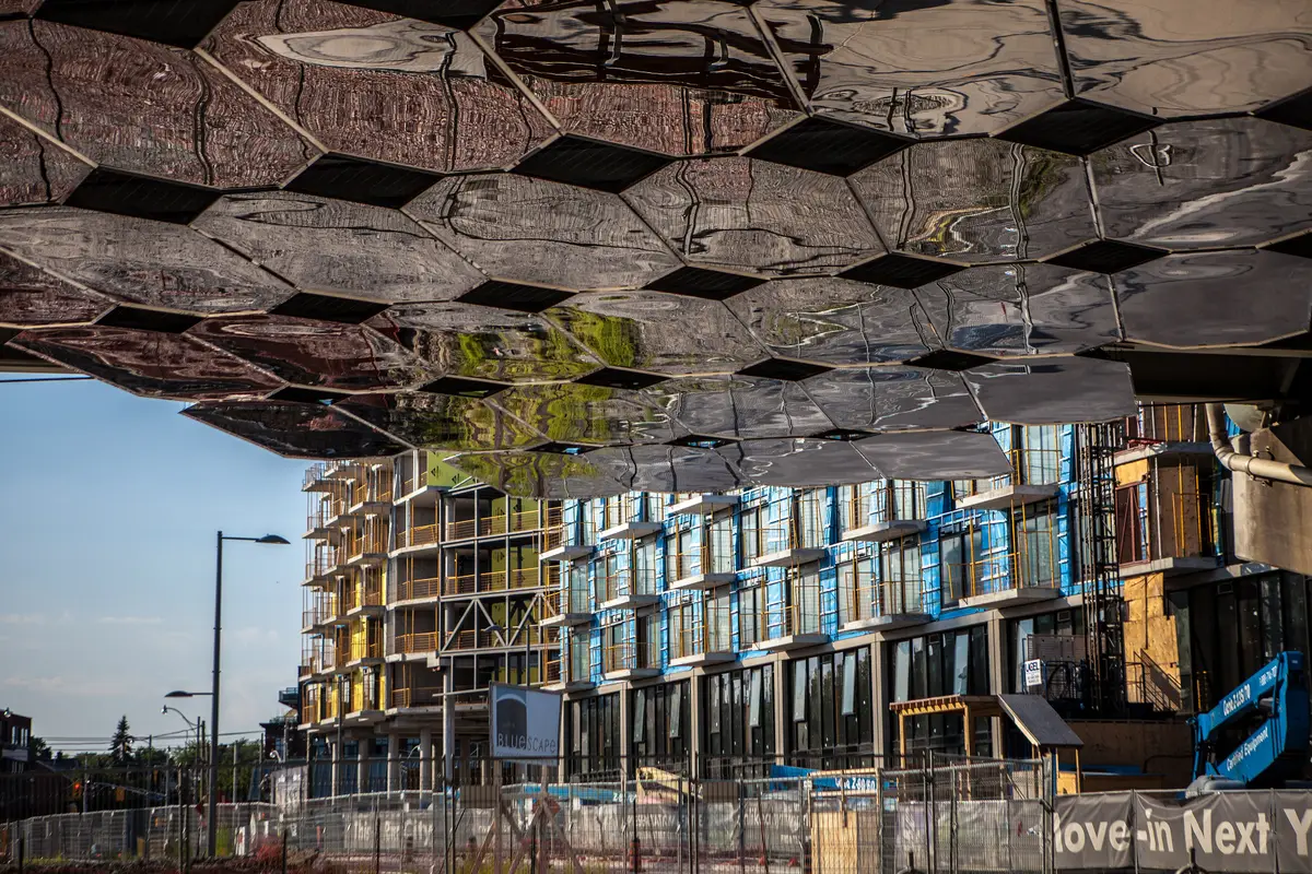 Hexagonal reflective panels on the underside of the overpass, mirroring the buildings beside it