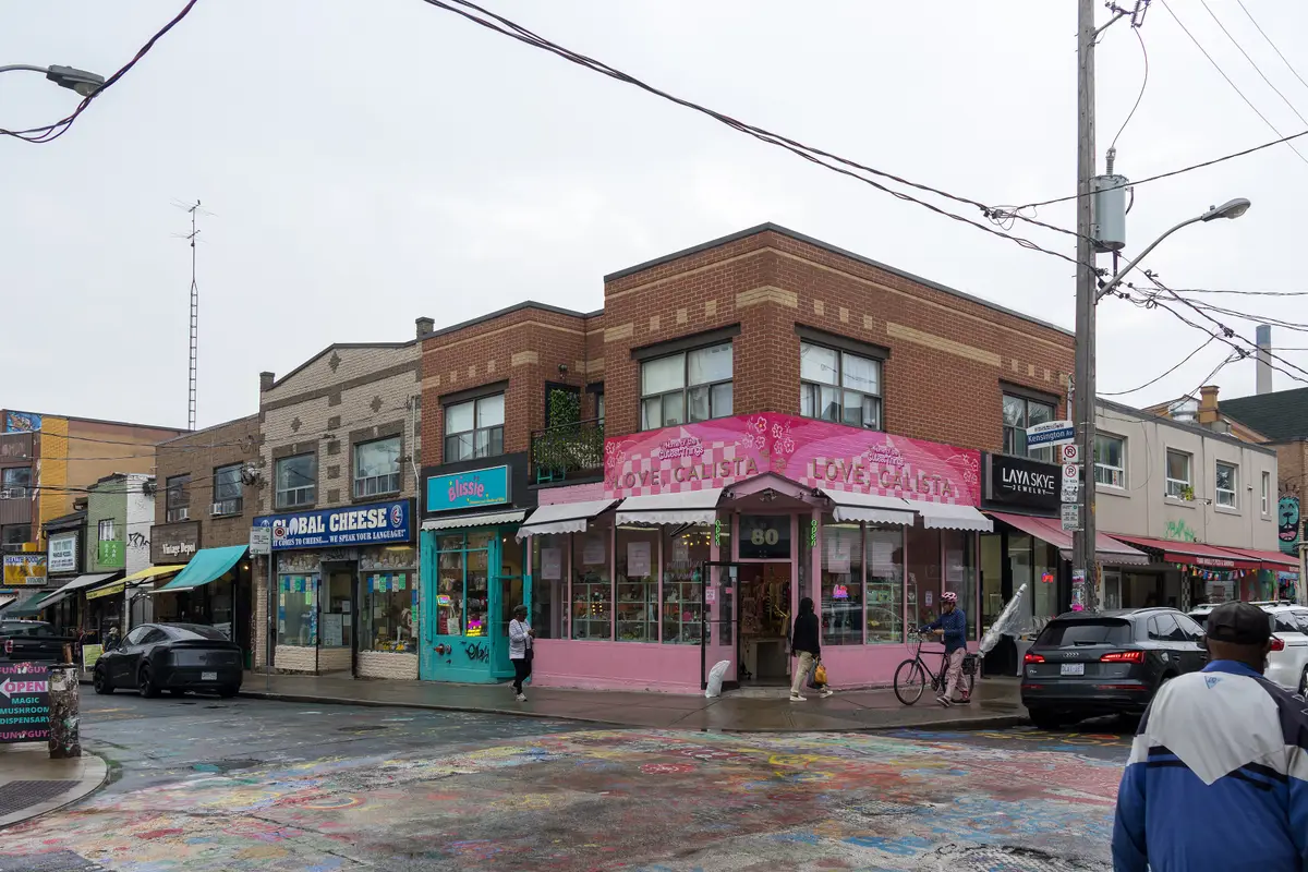 Brightly painted shopfronts on a corner of Kensington Market on an overcast day, with people walking past
