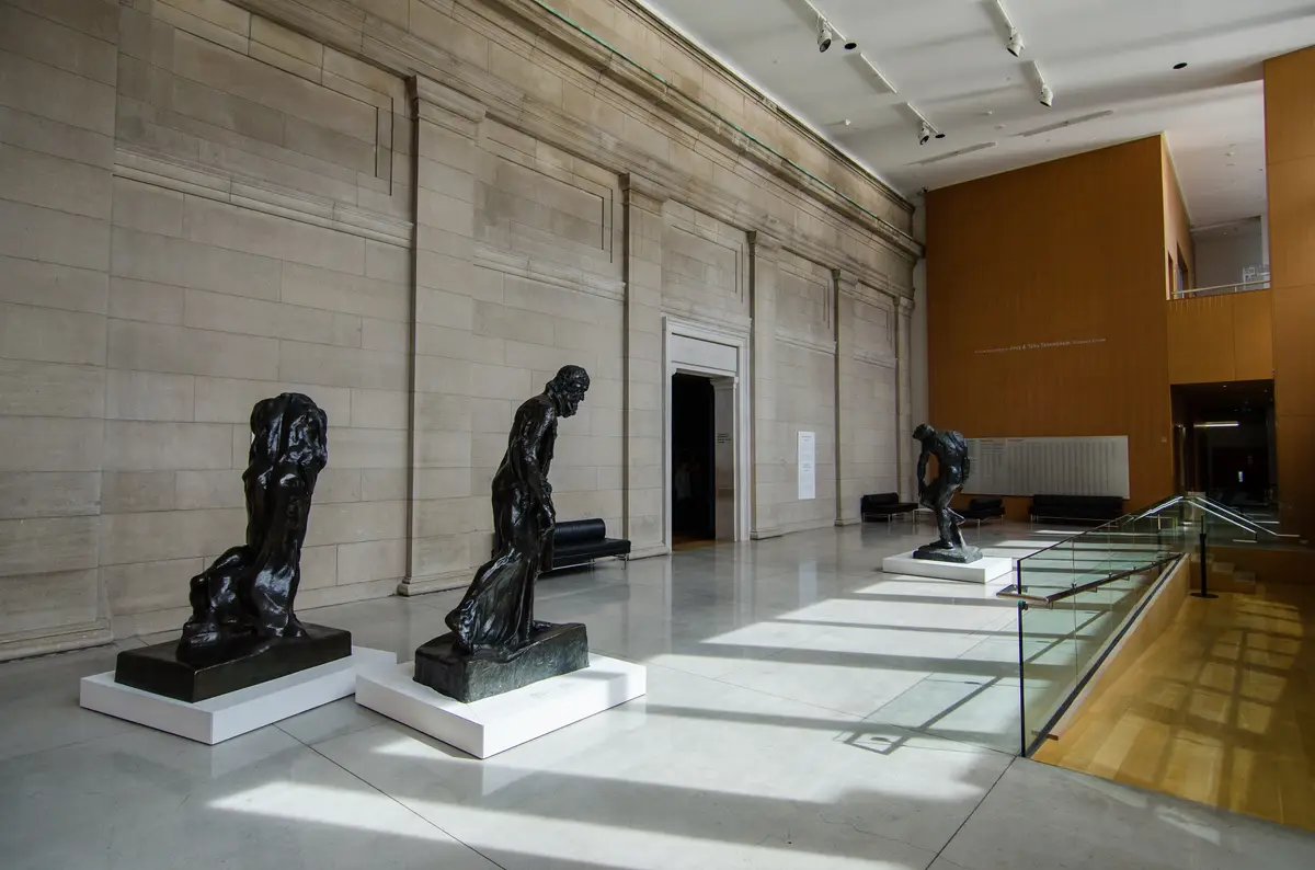 Three dark bronze sculptures on white plinths in a bright stone-walled gallery hall