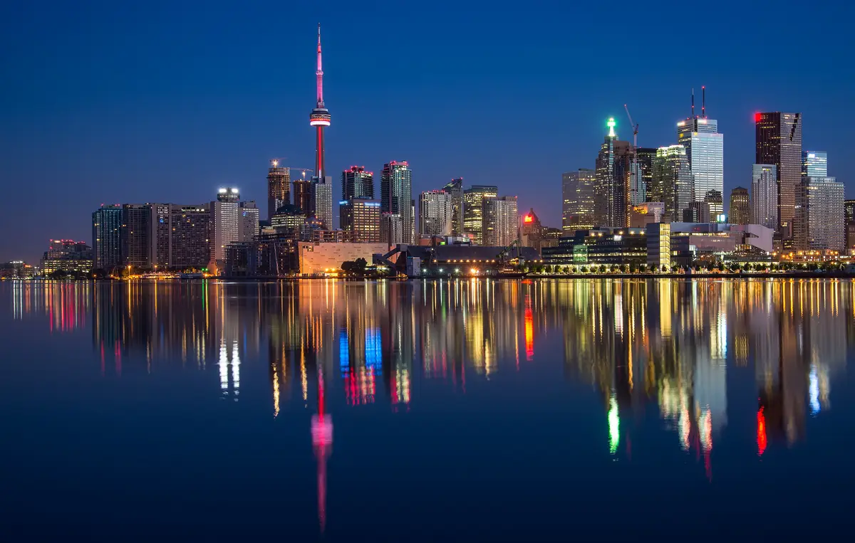 The Toronto skyline lit up at night, with the CN Tower and towers reflected in calm water