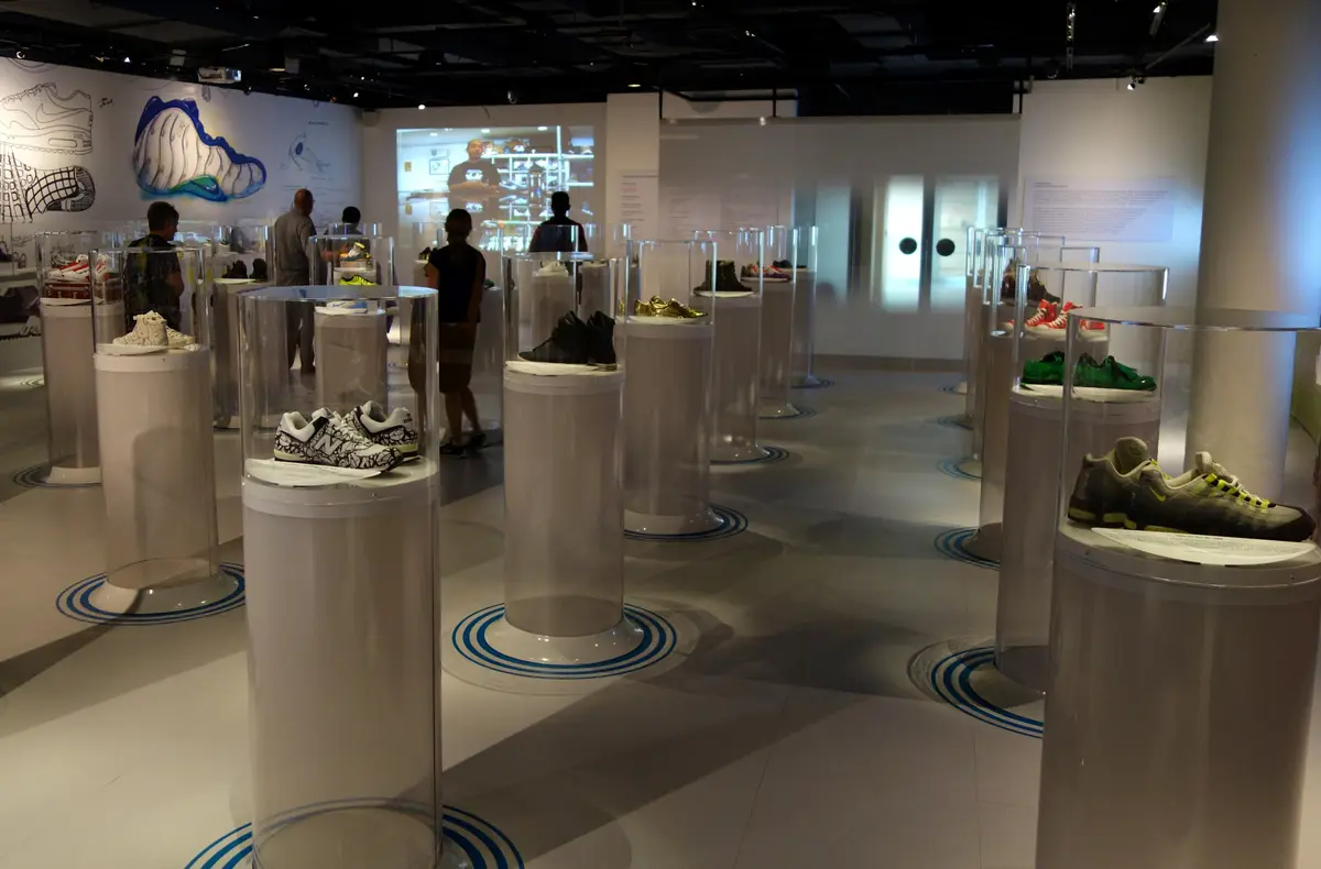 Sneakers on display in clear cylinder cases in a gallery at the Bata Shoe Museum, with visitors among the cases