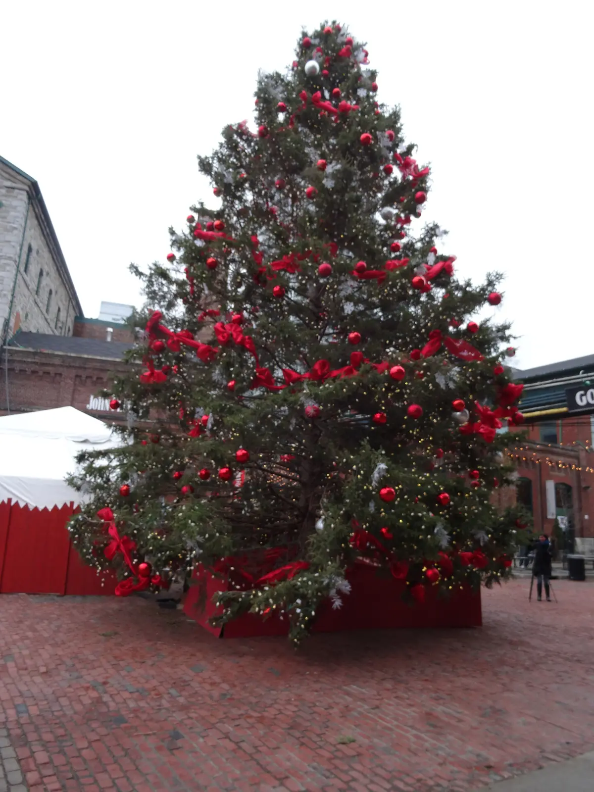 A tall Christmas tree decorated with red ribbons on a brick-paved lane in the Distillery District
