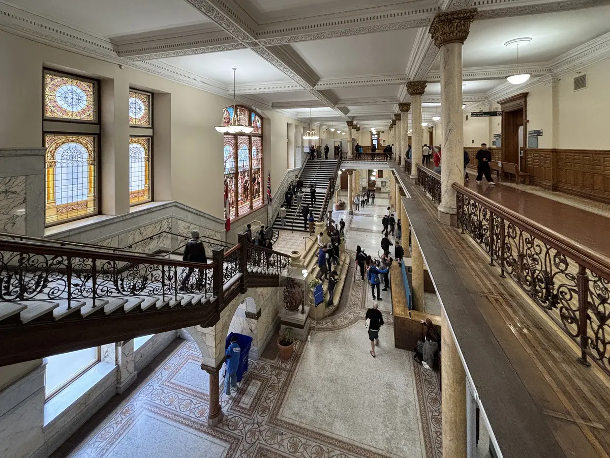 The grand lobby of Old Toronto City Hall, with a wide staircase, stained-glass windows and a patterned tile floor