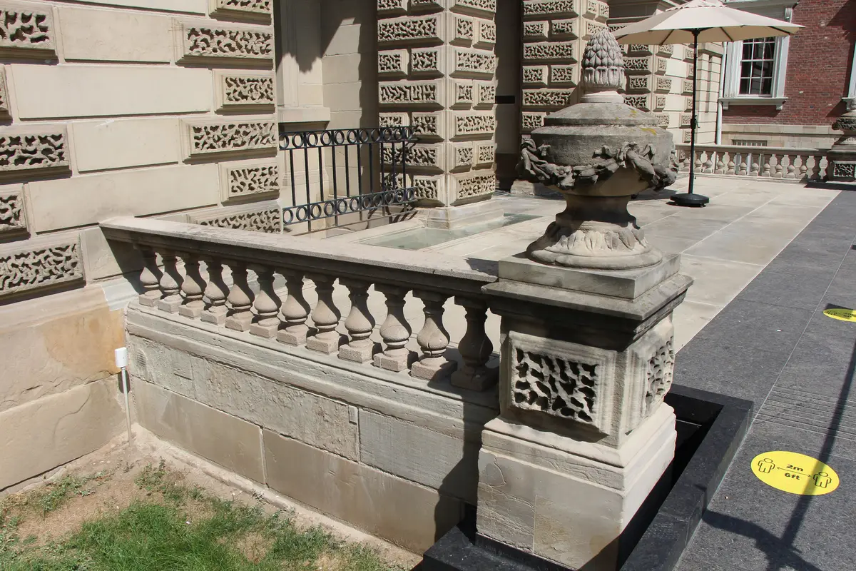 A carved stone balustrade and urn at Osgoode Hall, with a black iron railing beside it