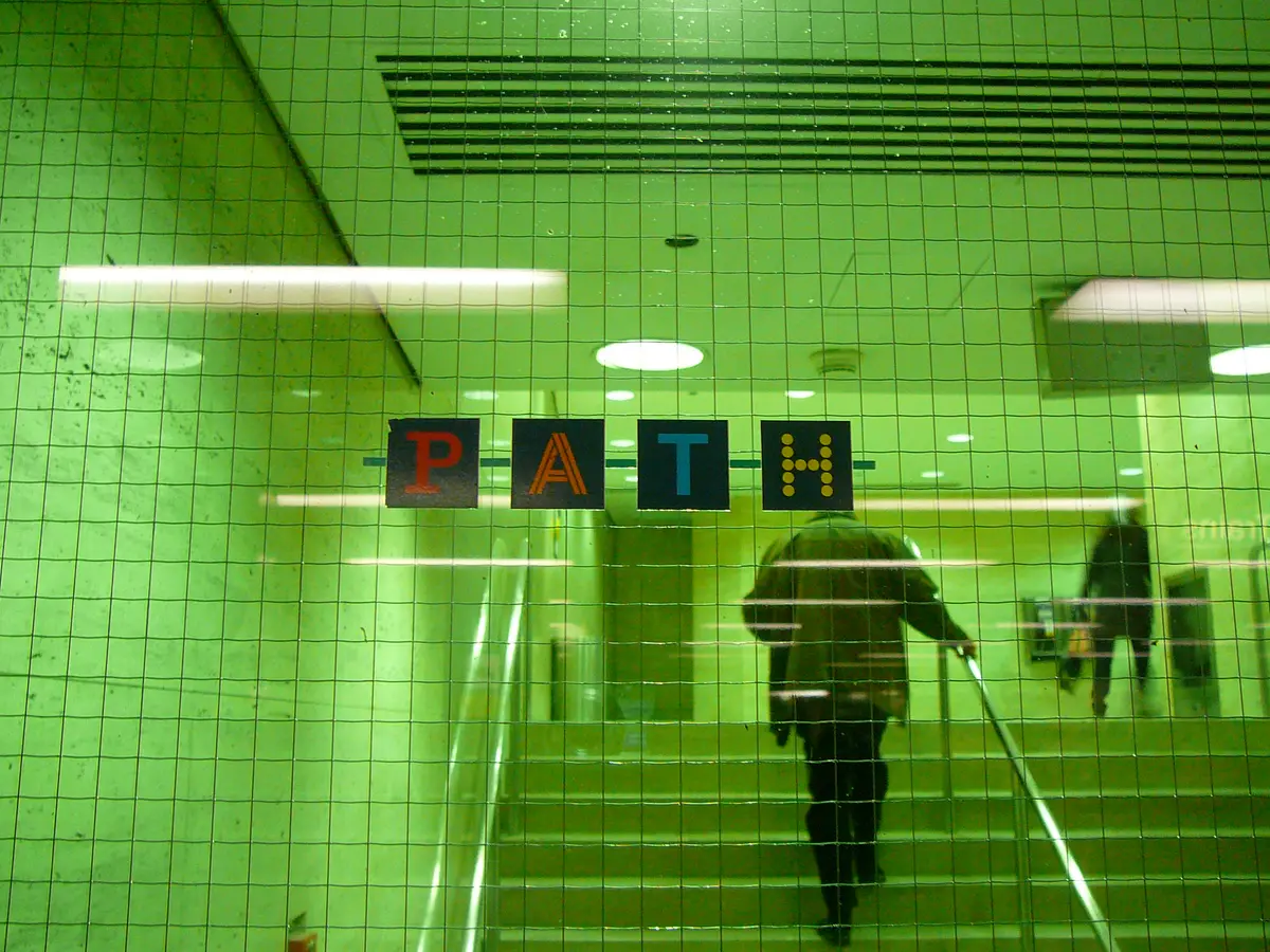 A green tiled PATH passage with PATH signs overhead and a pedestrian climbing the stairs