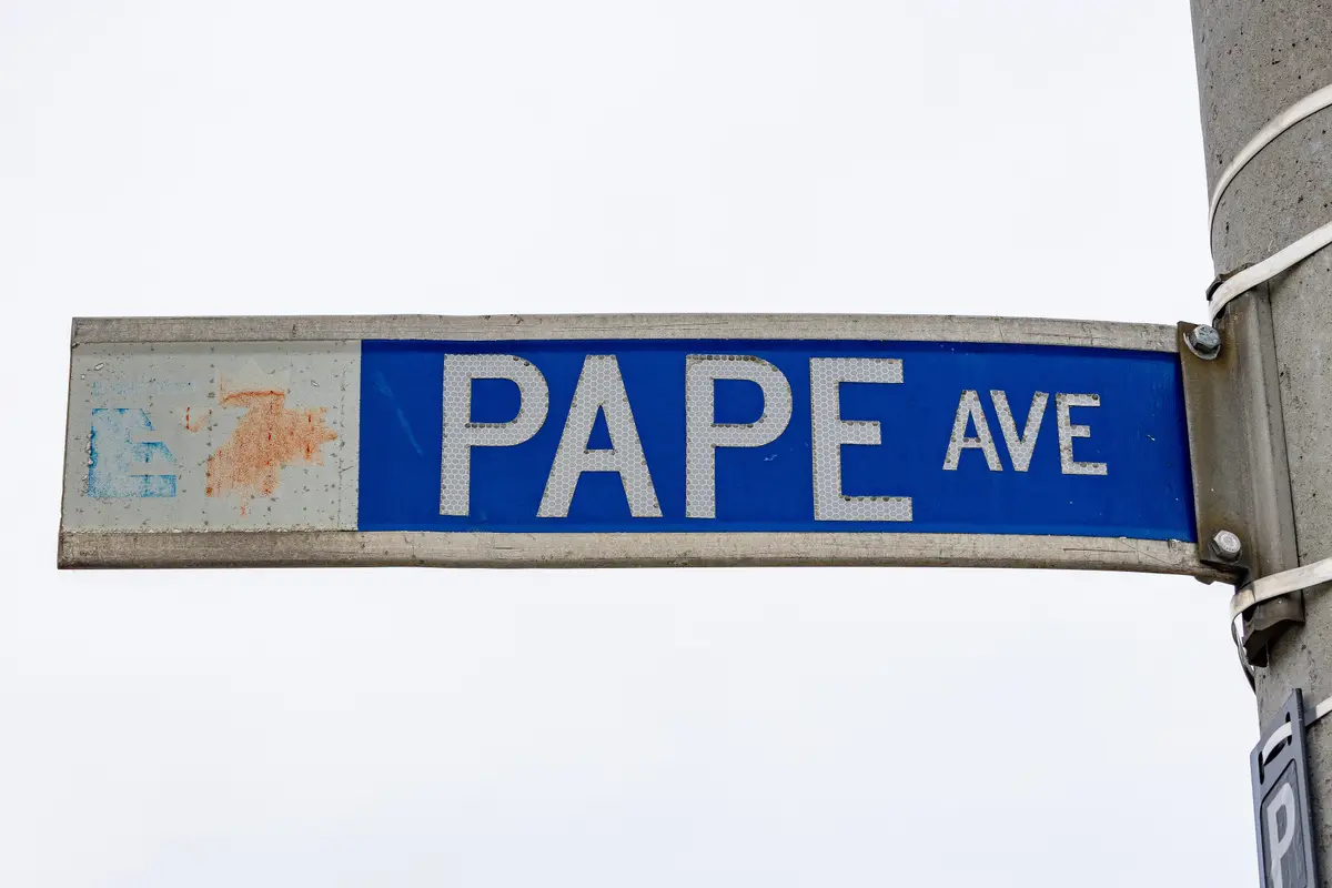 A blue Pape Avenue street sign with a faded East York logo on a grey pole against an overcast sky