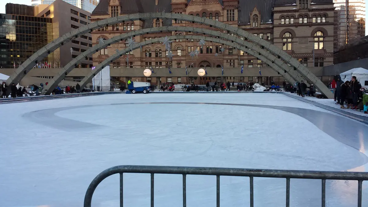 An outdoor skating rink with curved arches and a stone civic building behind it.