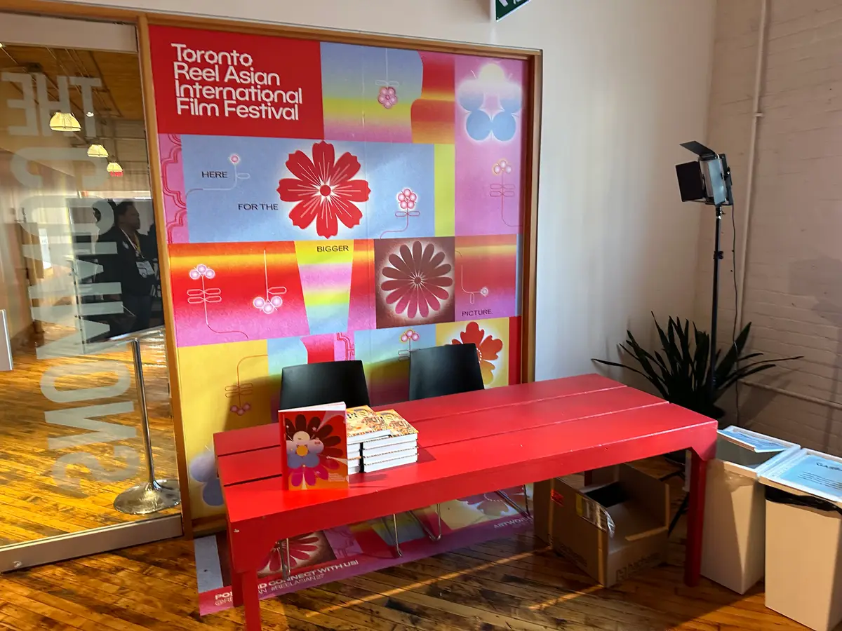 A red bench with booklets in front of a Toronto Reel Asian International Film Festival banner