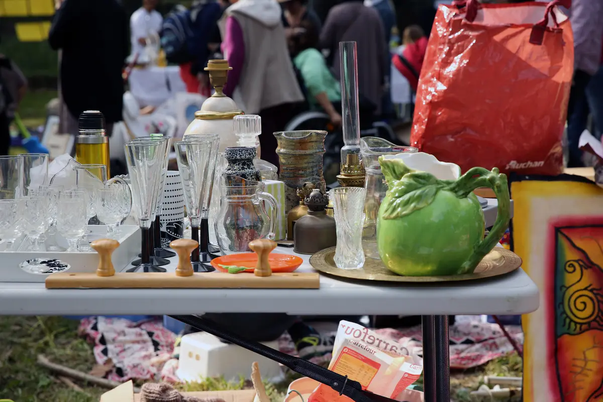 A sale table with stemmed glasses, a green ceramic jug and a brass tray at an outdoor spring flea market.