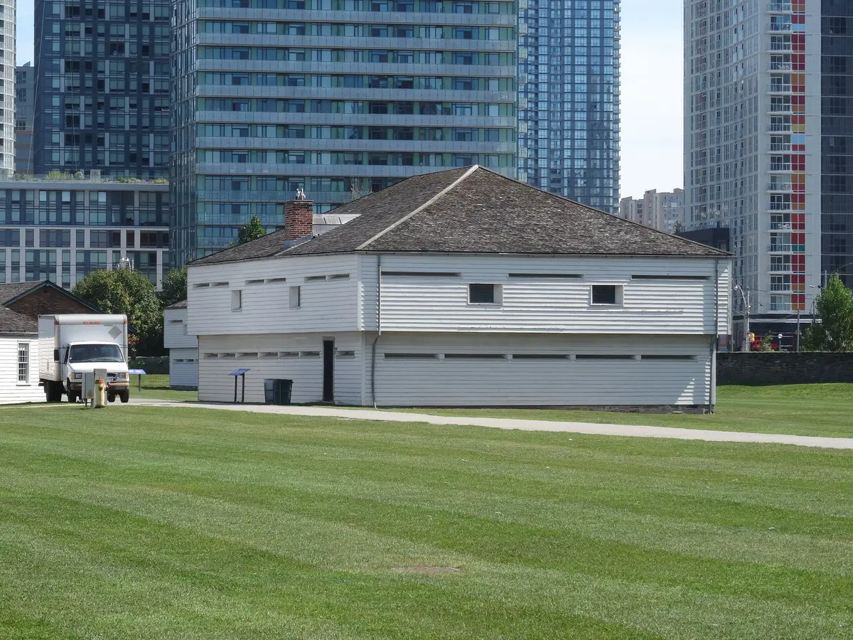 One of Fort York's two blockhouses, a white wooden building on a sunny lawn, with condo towers rising behind