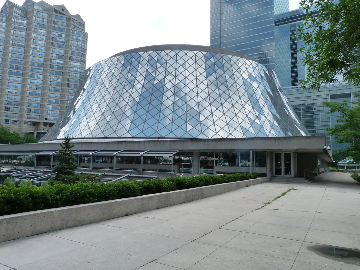 The glass-faceted dome of Roy Thomson Hall seen from a paved plaza between downtown towers