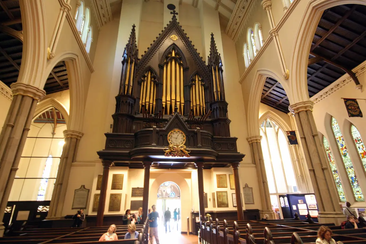 A tall pipe organ case with gold pipes at the end of a cathedral nave, with pews and stained glass