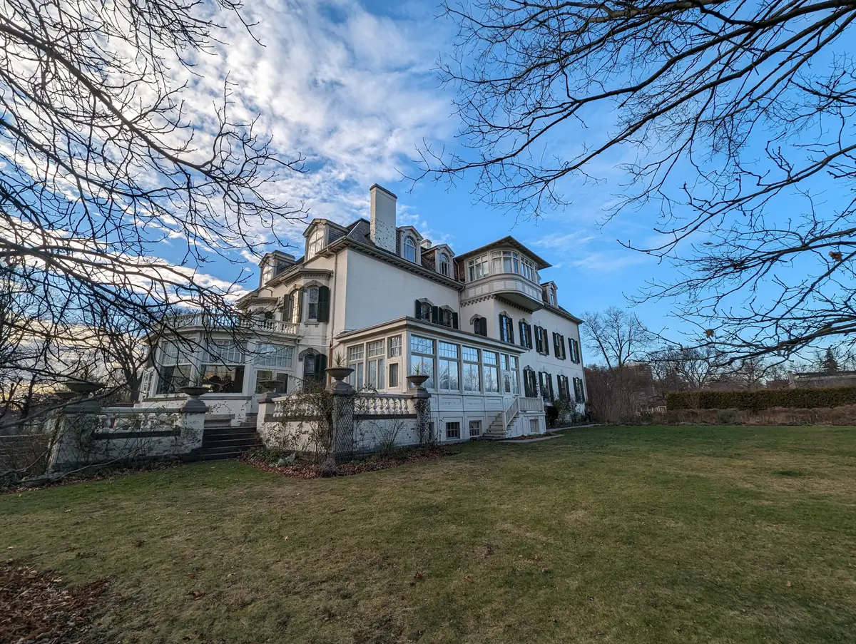 The white garden-side facade of Spadina House seen across a lawn, with bare trees and blue sky.