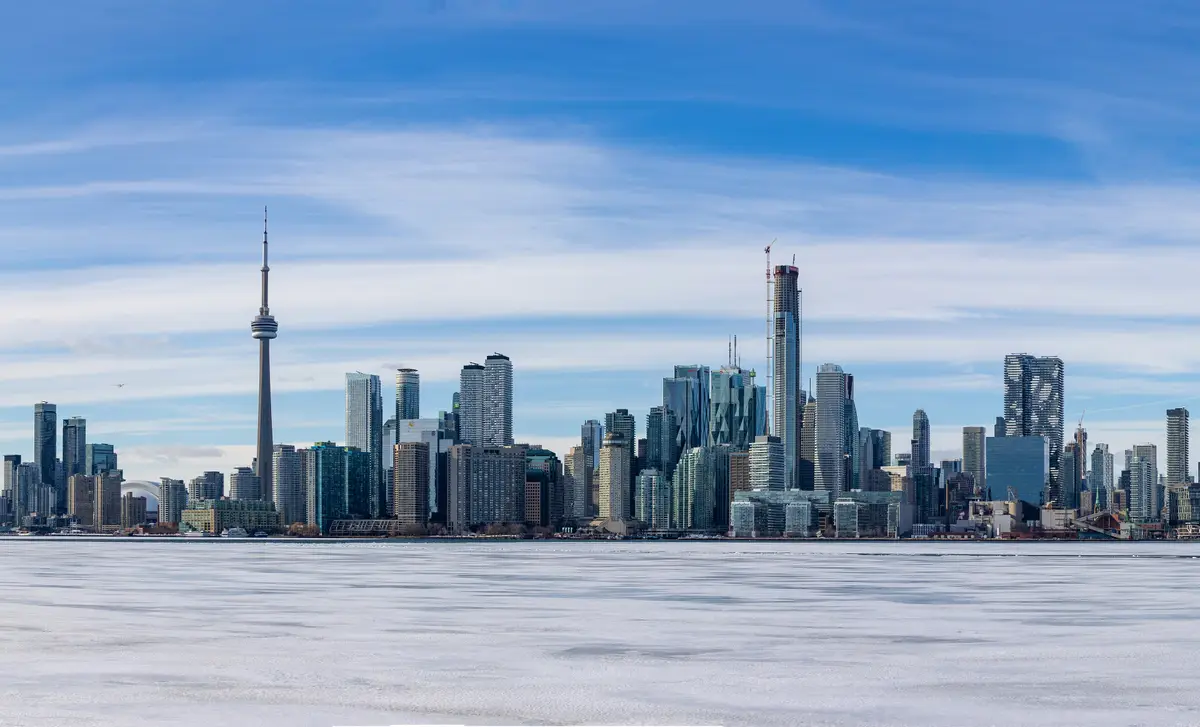The Toronto skyline and CN Tower behind a frozen, snow-dusted lake under streaky blue sky