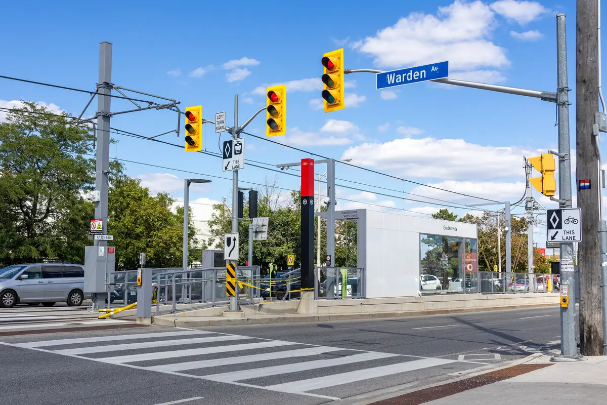 The Golden Mile Line 5 stop on Eglinton Avenue East at Warden Avenue, with overhead wires and a station shelter under a blue sky.