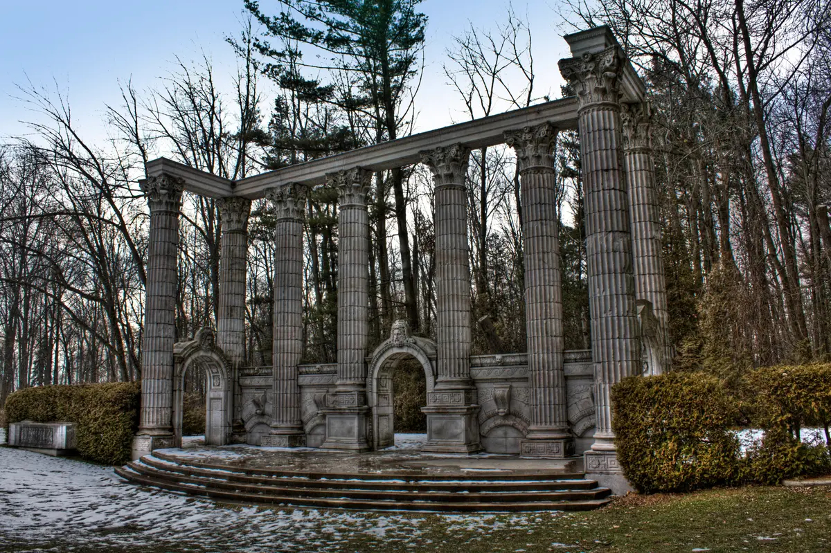 Weathered stone columns, arches and steps of the Greek Theatre at Guild Park, framed by bare trees in winter.